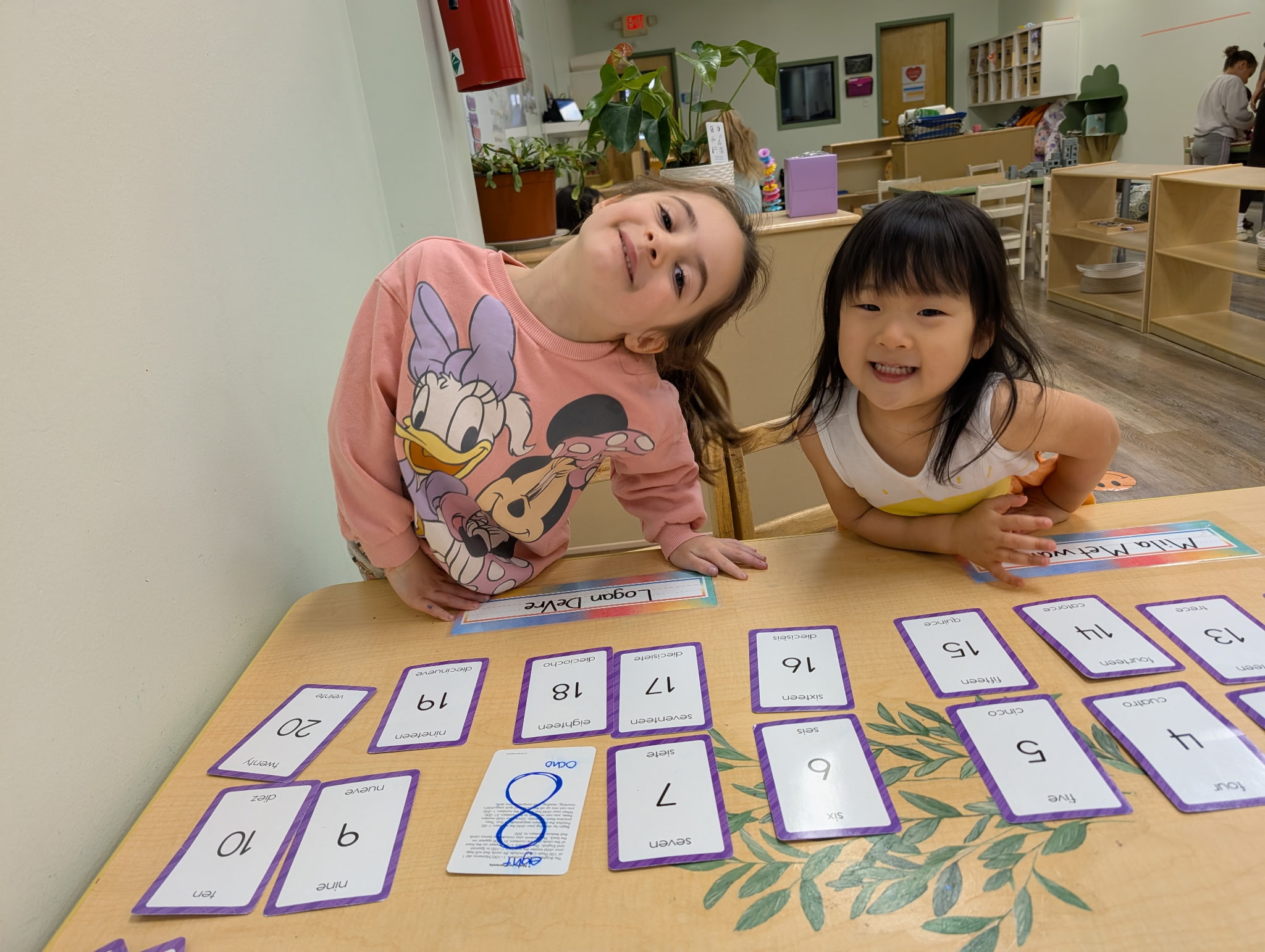 Two preschool girls smiling over number cards at Mighty Sprouts